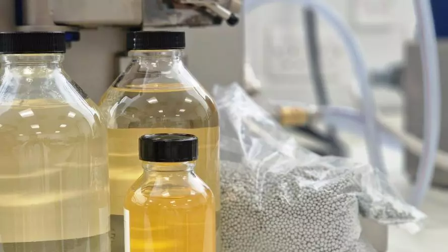 Bottles of various sizes containing yellow liquid and a bag of grey pellets behind