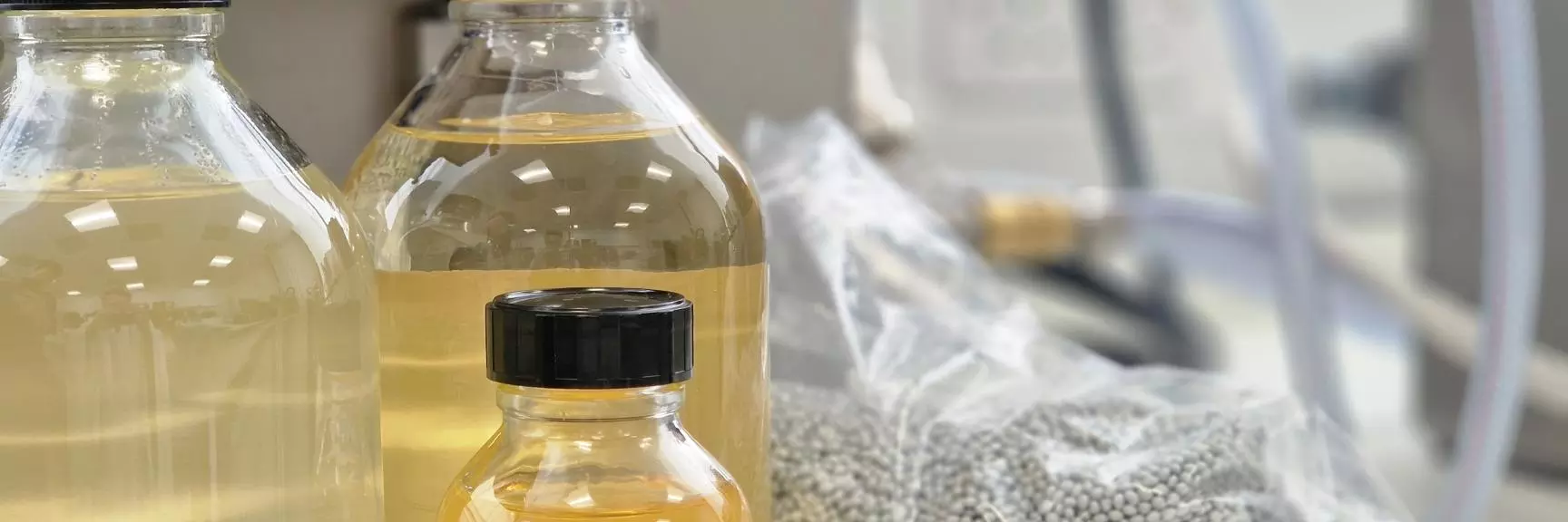 Bottles of various sizes containing yellow liquid and a bag of grey pellets behind